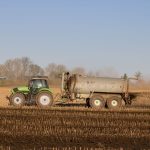 Trator com tanque aplicando fertilizante sobre uma área agrícola.