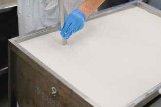 Trabalhador utiliza uma ferramenta durante a produção artesanal de queijo em uma unidade de laticínios.