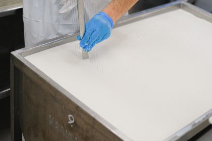 Trabalhador utiliza uma ferramenta durante a produção artesanal de queijo em uma unidade de laticínios.